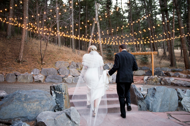 A bride and groom walk down a path under string lights, captured by Denver wedding photographer, Two One Photography.