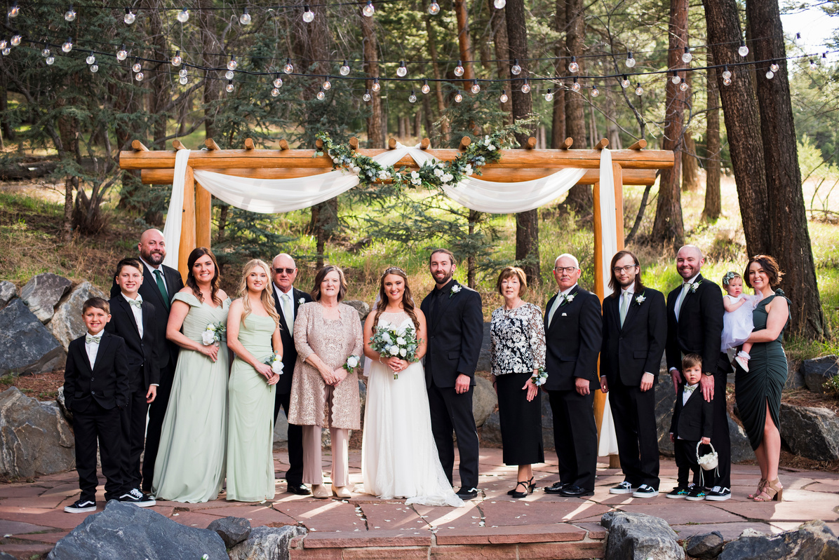 A wedding party poses for a photo in the woods at The Pines at Genesee in Genesee, Colorado.