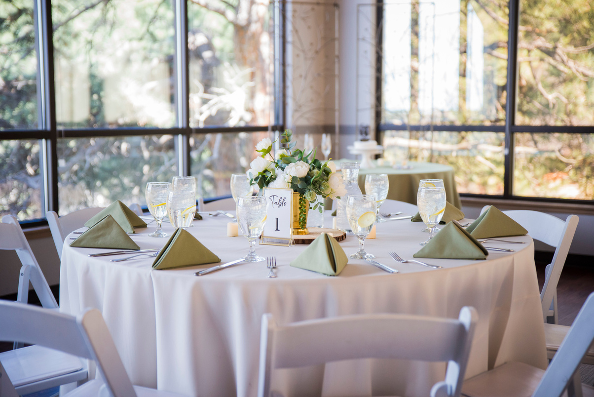 A round table with white chairs and green napkins at the reception space at The Pines at Genesee.