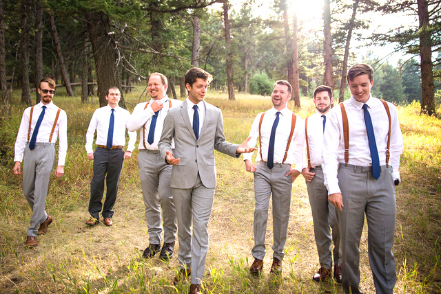 A group of groomsmen candidly walking toward the camera in the woods.