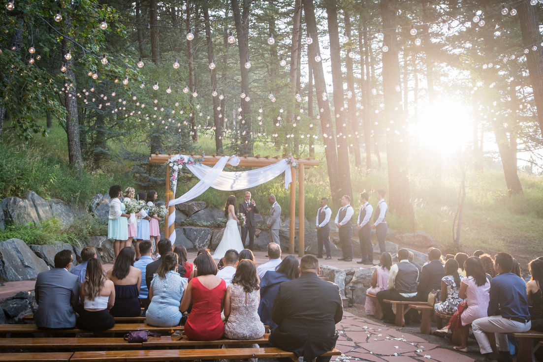 A wedding ceremony in the woods with string lights at The Pines at Genesee in Genesee, Colorado.